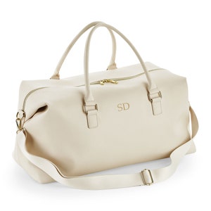 May include: A cream-colored leather travel bag with a gold zipper and a gold strap. The bag has a monogram "SD" on the front.