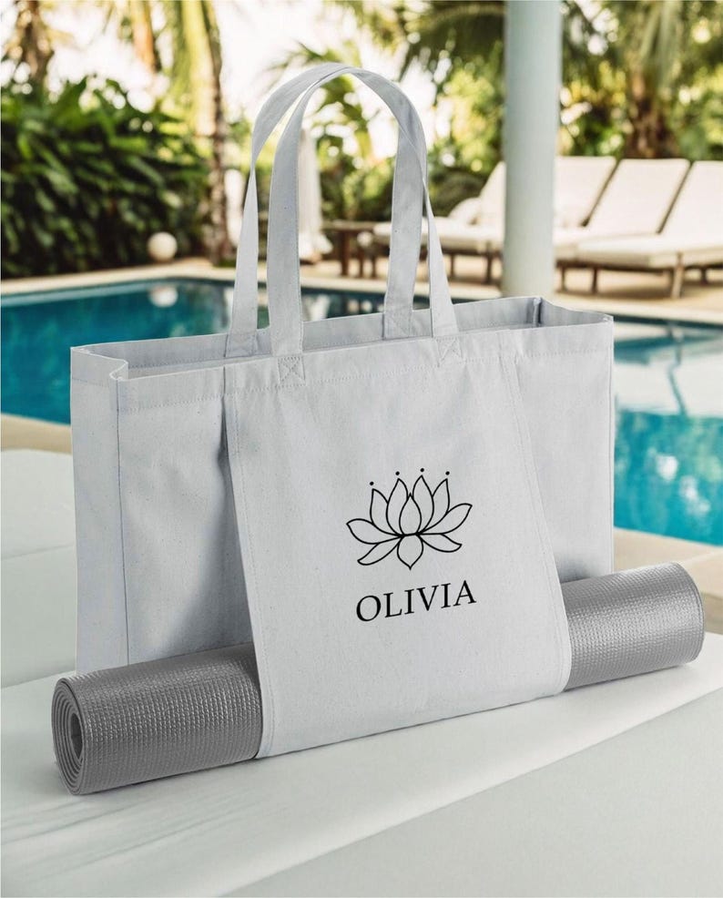 A white tote bag with a black logo and text, placed on a gray mat, with a pool and palm trees in the background.
