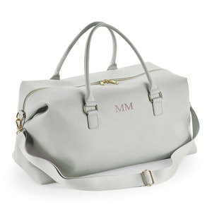 May include: A light gray leather duffel bag with a gold zipper and gold hardware. The bag has a long shoulder strap and two top handles. The initials "MM" are embroidered on the front of the bag.