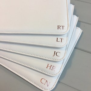 May include: Five white zippered pouches with rose gold initials, RT, LT, JC, HR, and CN, stacked on top of each other.