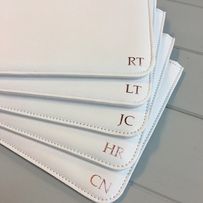 May include: Five white zippered pouches with rose gold initials, RT, LT, JC, HR, and CN, stacked on top of each other.