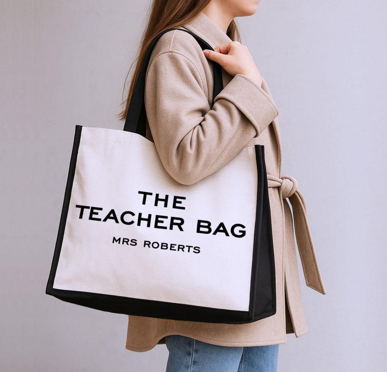 A woman wearing a beige coat is carrying a large white bag with black text that says "THE TEACHER BAG MRS ROBERTS".