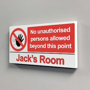 Puede incluir: Un letrero rectangular blanco con borde y texto en rojo. A la izquierda hay un símbolo de prohibición rojo con una mano negra. El texto dice: No unauthorised persons allowed beyond this point. Debajo de una línea negra, dice: Jack's Room.