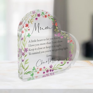 Puede incluir: Un recuerdo en forma de corazón de acrílico transparente con detalles florales. El texto dice "Mum" y un mensaje de amor. Los bordes están adornados con un diseño floral en acuarela en tonos rojos, morados y verdes. Un regalo conmovedor.