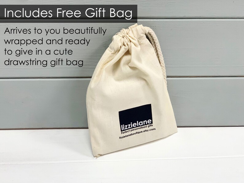 A beige drawstring gift bag with a black logo and text, placed on a white surface against a gray background.