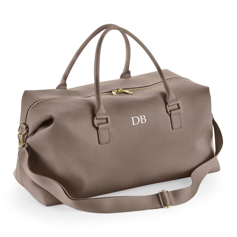 May include: A brown leather travel bag with a gold zipper and a gold strap. The bag has a white monogram "DB" on the front.