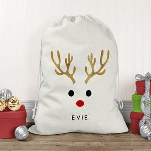 May include: A white drawstring gift sack featuring a gold reindeer antler graphic, two black circular eyes, a red circular nose, and the name EVIE printed in black capital letters centred below the reindeer face design.