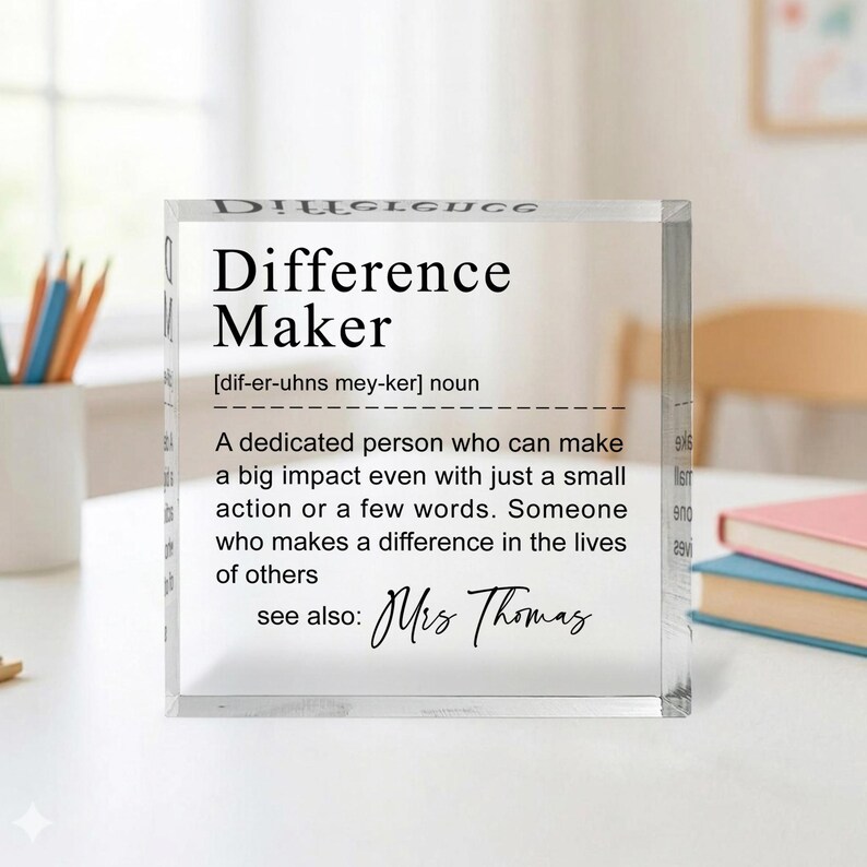 A clear glass block with a definition of a " Difference Maker" written on it, along with a quote about a teacher named Mrs. Thomas.