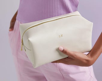 May include: A cream-colored rectangular cosmetic bag with a textured surface and a gold-toned zipper closure. The front of the bag features the letters LR embossed in a simple serif font. The bag has a structured shape with gusseted sides.