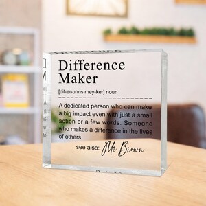 A clear glass block with the definition of a " Difference Maker" written on it, along with a quote attributed to Mr. Brown.