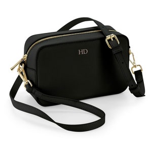 May include: A black leather crossbody bag with a gold zipper and buckle. The bag has a gold chain strap and the initials "HD" are embossed on the front.