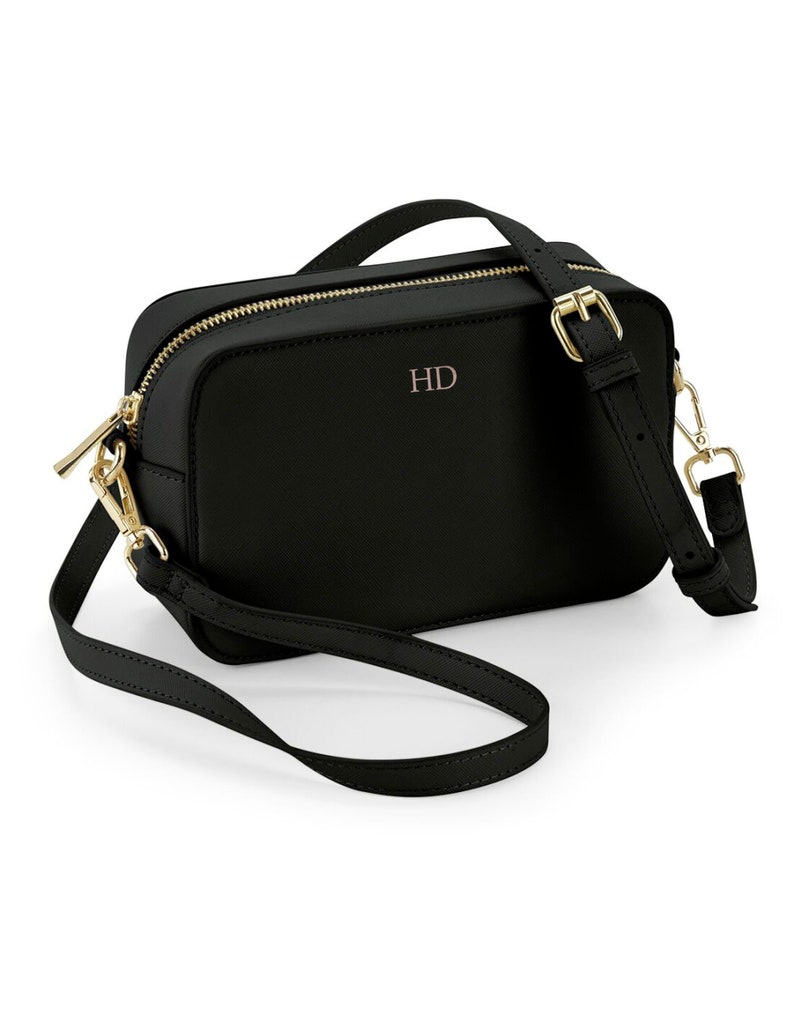May include: A black leather crossbody bag with a gold zipper and buckle. The bag has a gold chain strap and the initials "HD" are embossed on the front.