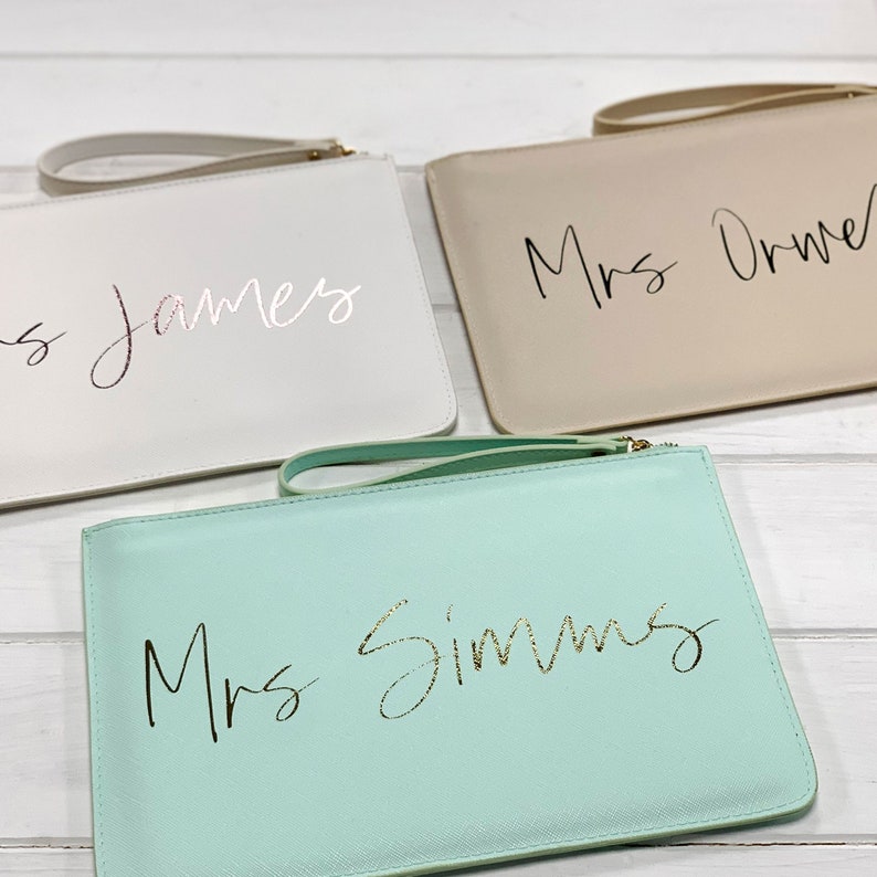 May include: Three clutches with different colored fabric and personalized with the text "Mrs. James", "Mrs. Orme", and "Mrs. Simms" in gold lettering.
