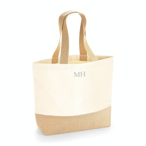 Pu&ograve; includere: Una borsa tote in tela beige con fondo in juta marrone. La borsa ha manici in tessuto marrone e le iniziali "MH" sono ricamate sul davanti in grigio.