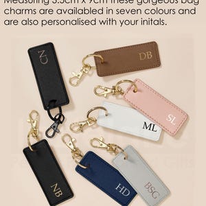 a collection of personalized bag charms, each with a unique initial printed on it. The charms are available in various colors and are designed to be attached to bags or accessories.