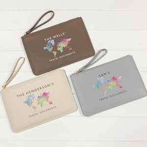 Könnte beinhalten: Drei rechteckige Reißverschlusstaschen mit Handschlaufen in Braun, Creme und Grau. Jede zeigt eine bunte Aquarell-Weltkarte, den Text TRAVEL DOCUMENTS sowie personalisierte Namen: THE WELLS', THE HENDERSON'S und SAM'S.