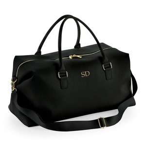 May include: Black leather travel duffel bag with a gold zipper and gold hardware. The bag has a shoulder strap and a personalized monogram that says "SD".