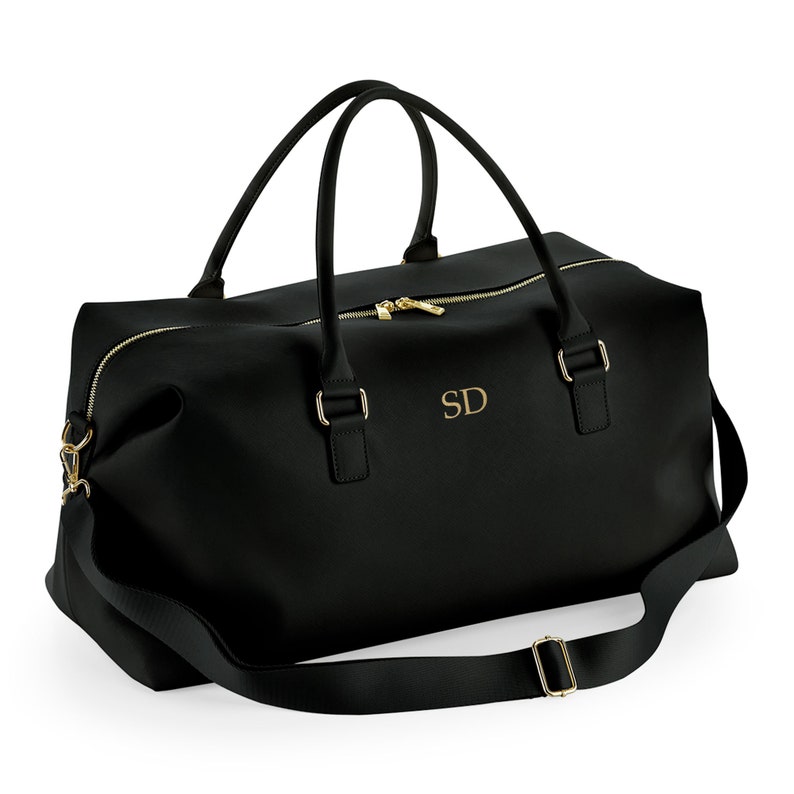 May include: Black leather travel duffel bag with a gold zipper and gold hardware. The bag has a shoulder strap and a personalized monogram that says "SD".