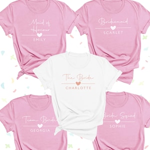 a collection of pink t-shirts with various names and titles printed on them, including "Maid of Honor", "Emilly", "Bridal Squad", "Team Bride", and "Charlotte".