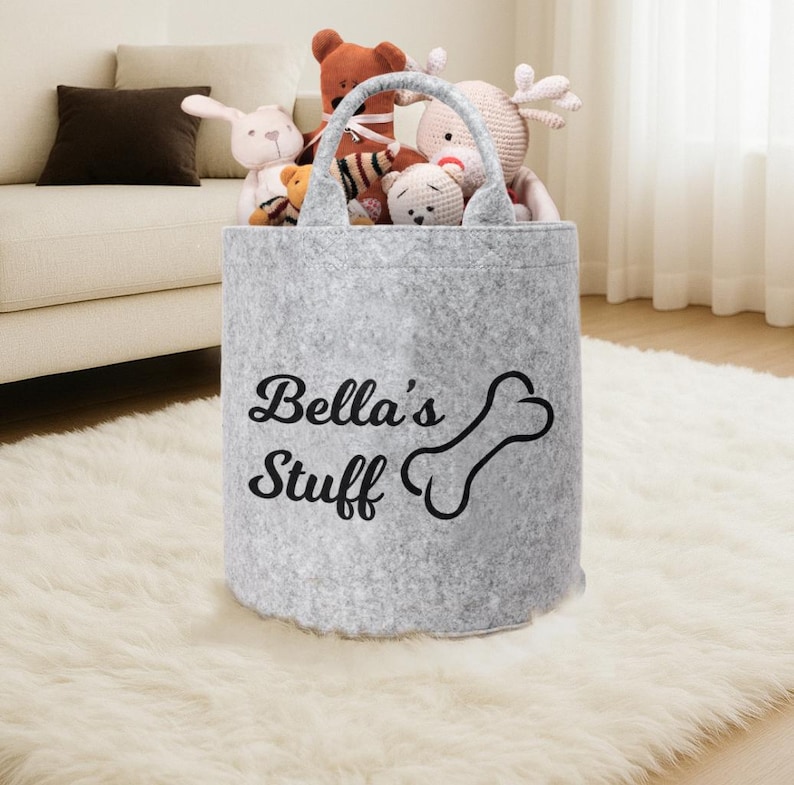 A gray felt storage bag with the text "Bella's Stuff" printed on it, filled with various stuffed animals.
