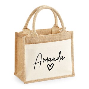 May include: A small, natural-colored burlap tote bag with a white canvas pocket. The pocket has the name "Amanda" written in black cursive with a small heart below it.