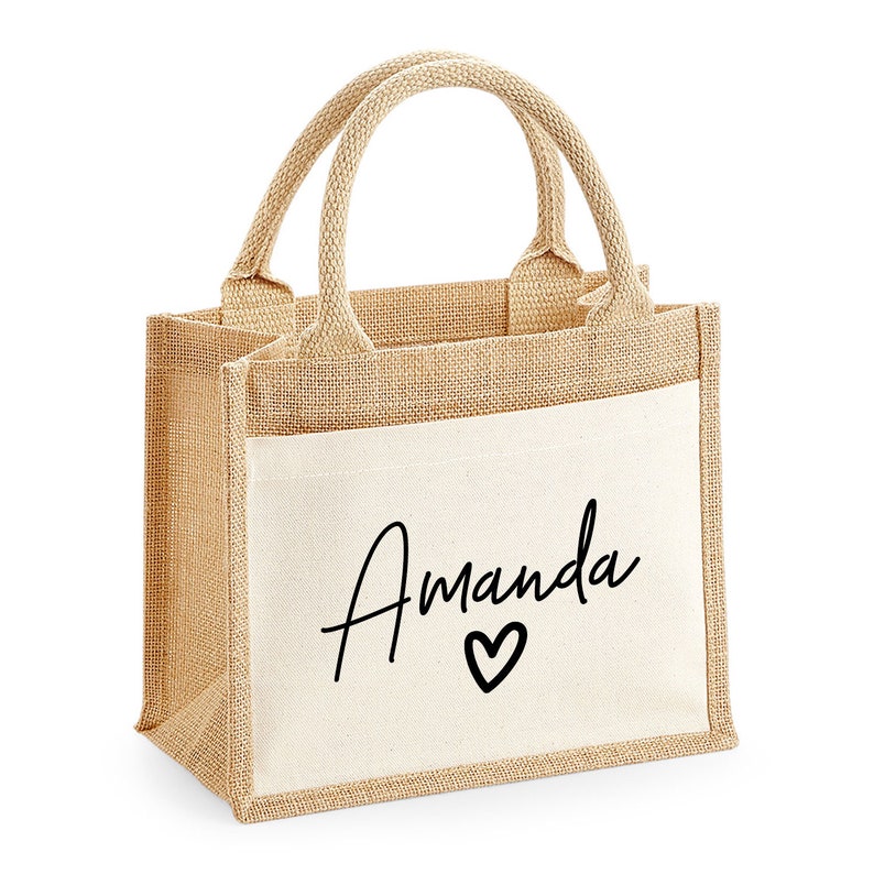 May include: A small, natural-colored burlap tote bag with a white canvas pocket. The pocket has the name "Amanda" written in black cursive with a small heart below it.