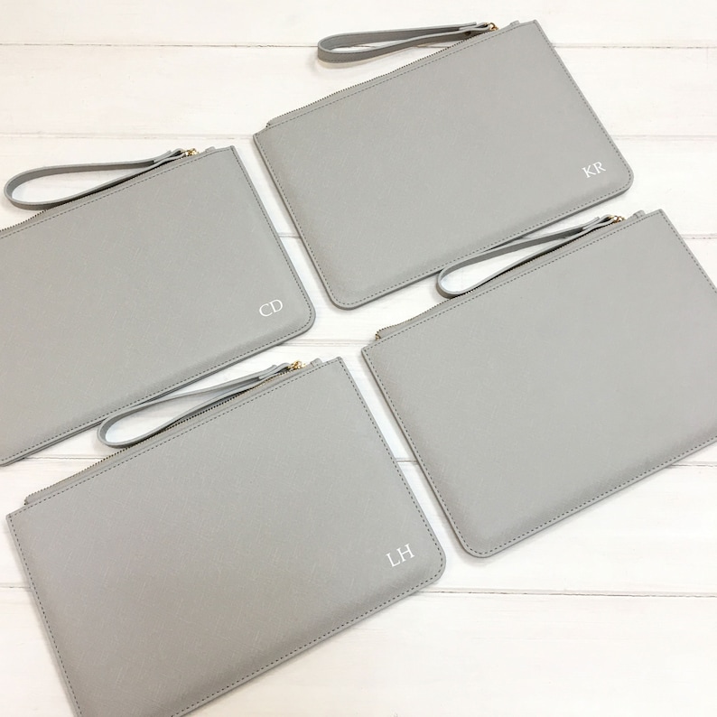 May include: Four gray zippered pouches with gold zippers and white leather handles. Each pouch has a different set of initials monogrammed on the front: CD, KR, LH.