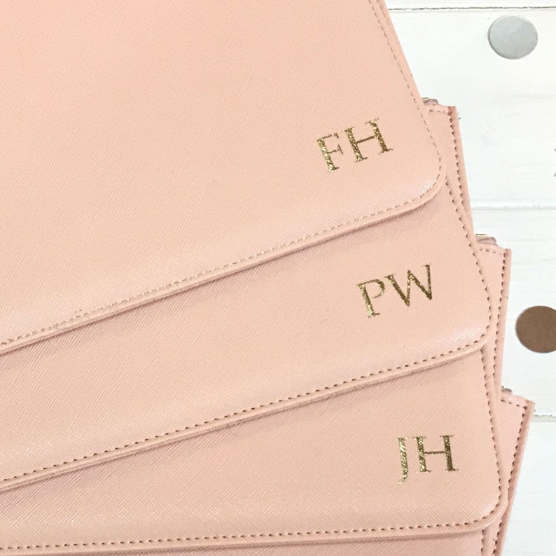 May include: Three pink leather pouches with gold lettering. The pouches are stacked on top of each other. The top pouch has the initials "FH" in gold lettering. The middle pouch has the initials "PW" in gold lettering. The bottom pouch has the initials "JH" in gold lettering.