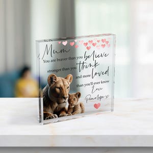 Może przedstawiać: Przezroczysty blok akrylowy z nadrukowanym obrazem lwicy i jej lwiątka. Tekst brzmi: Mum, You are braver than you believe, stronger than you think, and more loved than you'll ever know. Love, Penelope x. Różowe serca zdobią górną część bloku.