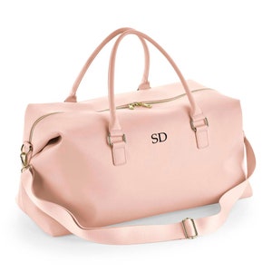 May include: A blush pink leather travel bag with a gold zipper and a gold strap. The bag has a monogrammed "SD" on the front.
