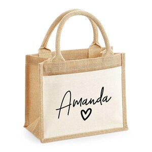 A beige tote bag with a printed name and heart design on it.
