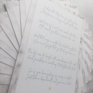 May include: A white card with a handwritten message about friendship. The card has a marble-like background and gold accents. The text reads: "If days like today have you feeling alone, just pop me a message or pick up the phone. And even if I can't come round or be there, I'll remind you there's someone who cares. And that way no matter how hard it might be, you won't forget that you'll always have me. This life can be tough with some bumps in the road, and friendship is something that lightens the load. So if you have feelings of worry or doubt, just take a deep breath and give me a shout."