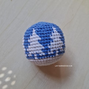 May include: A spherical crochet ball featuring a blue and white pattern of stylized evergreen trees. The base of the sphere is white, and the text LHYARNDESIGN is printed in white in the lower right corner of the image area.