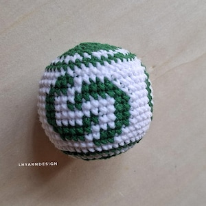 Puede incluir: Una pelota de ganchillo esférica con fondo blanco y un patrón en forma de hoja de color verde oscuro. El tejido es denso y texturizado, creando una forma redondeada. El texto LHYARNDESIGN está impreso en blanco abajo a la izquierda.