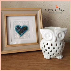 May include: A white ceramic owl oil burner with a heart-shaped design on a wooden surface. The owl has a cutout design and is a home fragrance item.