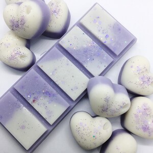 May include: A set of lavender and white heart-shaped wax melts with glitter. The wax melts are arranged around a larger lavender and white wax melt bar with six individual squares.