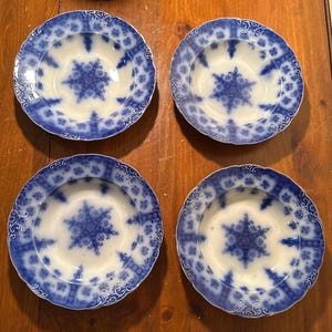 May include: Four antique blue and white porcelain bowls. Each bowl features a central starburst design and a decorative border. The bowls are arranged on a wooden surface, showcasing their intricate patterns and vintage charm.