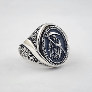 May include: A silver ring with an ornate design featuring a black cameo of the Grim Reaper holding a scythe.