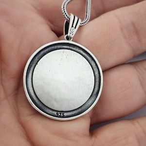 May include: A circular silver pendant with a textured edge and a plain centre, suspended from a silver chain. The pendant is stamped with the number "925" and the bail with "1925".