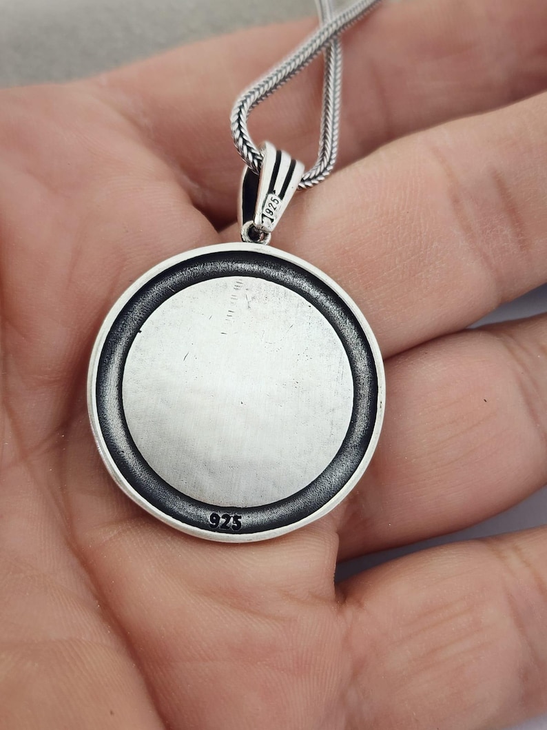 May include: A circular silver pendant with a textured edge and a plain centre, suspended from a silver chain. The pendant is stamped with the number "925" and the bail with "1925".