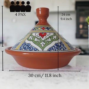 May include: A terracotta tagine with a conical lid featuring hand-painted floral and geometric patterns in red, green, blue, and yellow. The base measures 11.8 inches wide, with a total height of 9.4 inches. It is labeled for 4 PAX capacity.