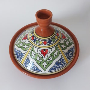 May include: A terracotta tagine with a conical lid featuring hand-painted geometric and floral patterns in red, green, blue, and yellow. The unglazed clay base contrasts with the glossy, multi-colored glazed lid, which has a central knob handle.