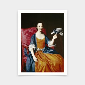 May include: A woman in a blue and orange dress sits in a red chair and holds a white bird in her right hand.