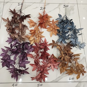 May include: Six different colored artificial leafy stems with a number and a hash symbol next to each stem. The stems are arranged in two rows of three. The colors are purple, red, orange, brown, blue, and green.