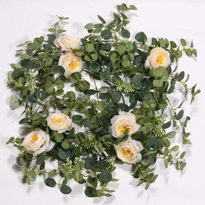 May include: A garland of artificial greenery featuring delicate, light pink roses. The garland includes eucalyptus leaves and small white berry clusters.
