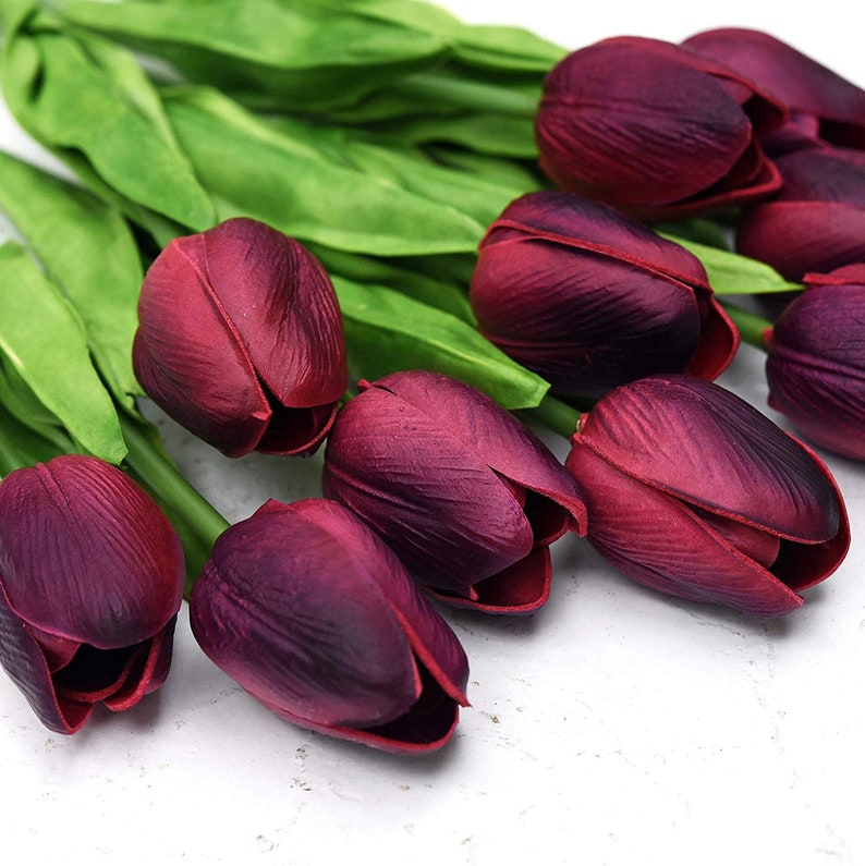 May include: A bouquet of artificial burgundy tulips with green stems. The tulips are arranged in a fan shape, with the tips of the flowers pointing towards the right side of the image.