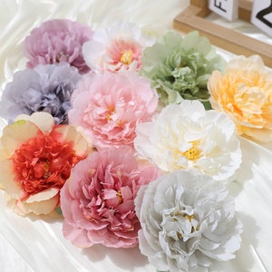 Puede incluir: Surtido de flores de peon&iacute;a artificiales en varios colores, incluyendo rosa, blanco, melocot&oacute;n, naranja, verde y gris. Las flores est&aacute;n hechas de tela y tienen un aspecto realista.