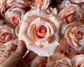 Puede incluir: Primer plano de un montón de rosas artificiales de color melocotón. Las rosas están hechas de tela y tienen un aspecto realista.
