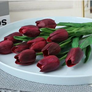 May include: A bouquet of artificial burgundy tulips with green stems arranged on a light blue round tray.