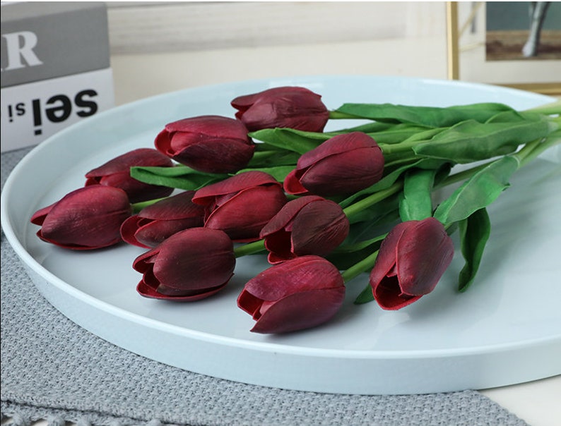 May include: A bouquet of artificial burgundy tulips with green stems arranged on a light blue round tray.